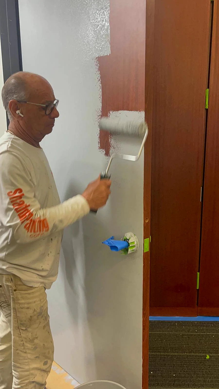 An El Shaddai painter rolling a wall in an office with the trim masked off