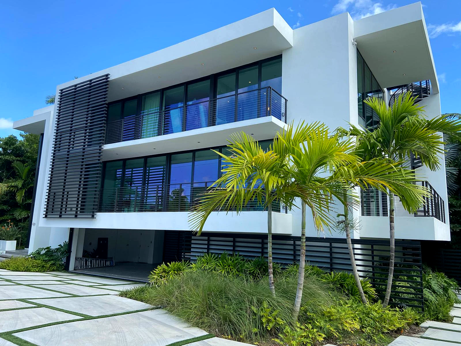 A three-story modern white home with black louvers and palms, freshly painted